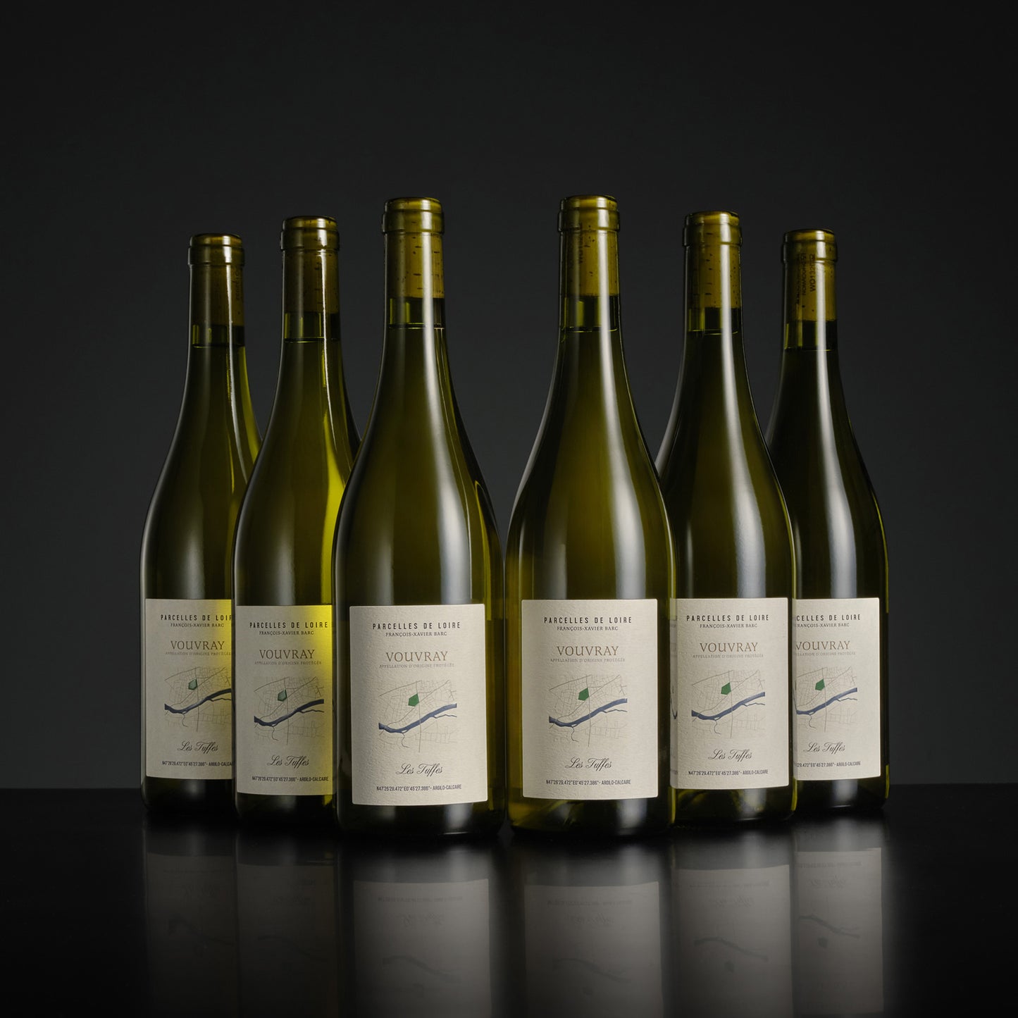 Six bottles of Vouvray wine lined up on a dark background