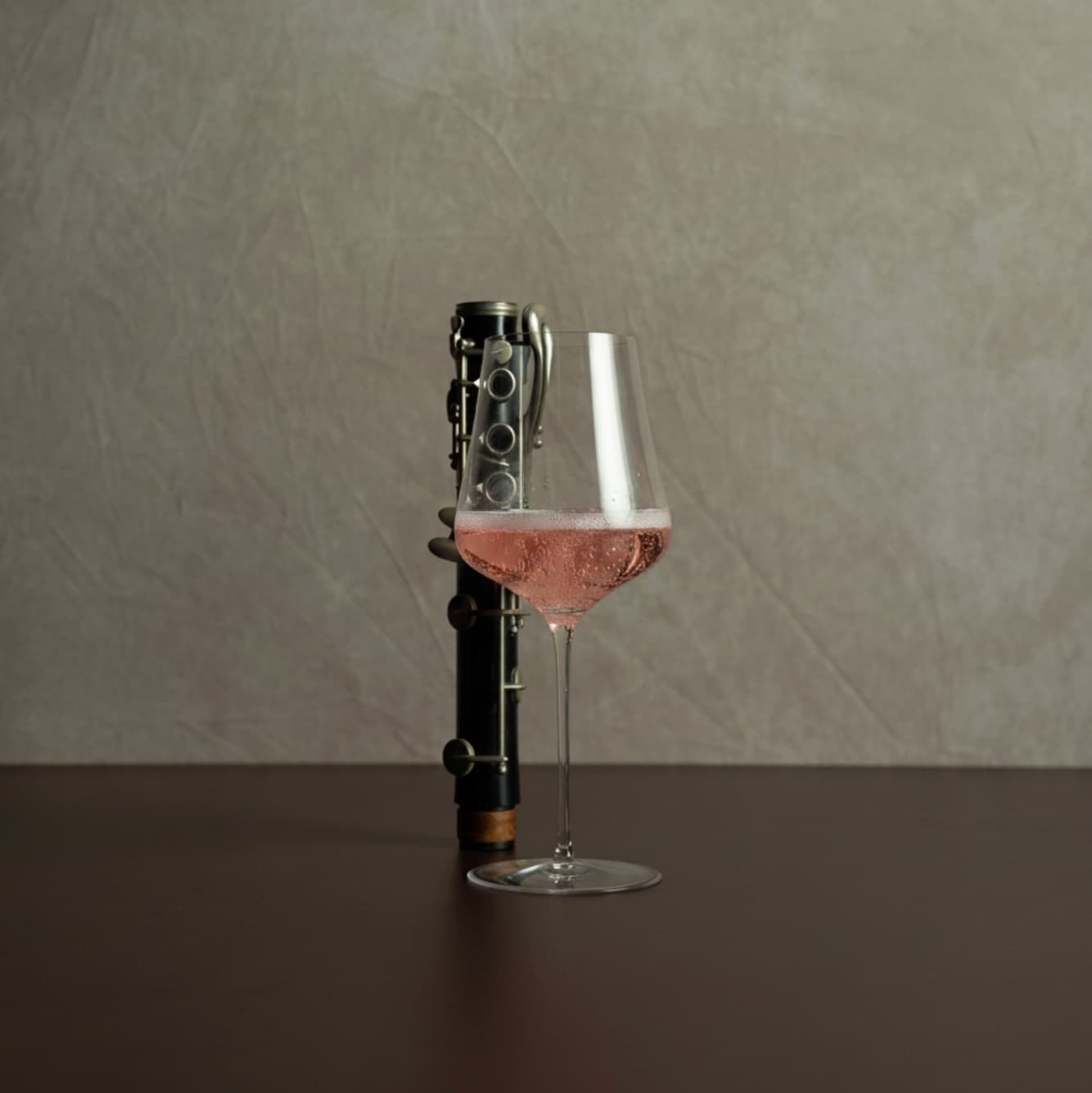 Wine glass with pink wine and bottle on a dark surface with a gray background