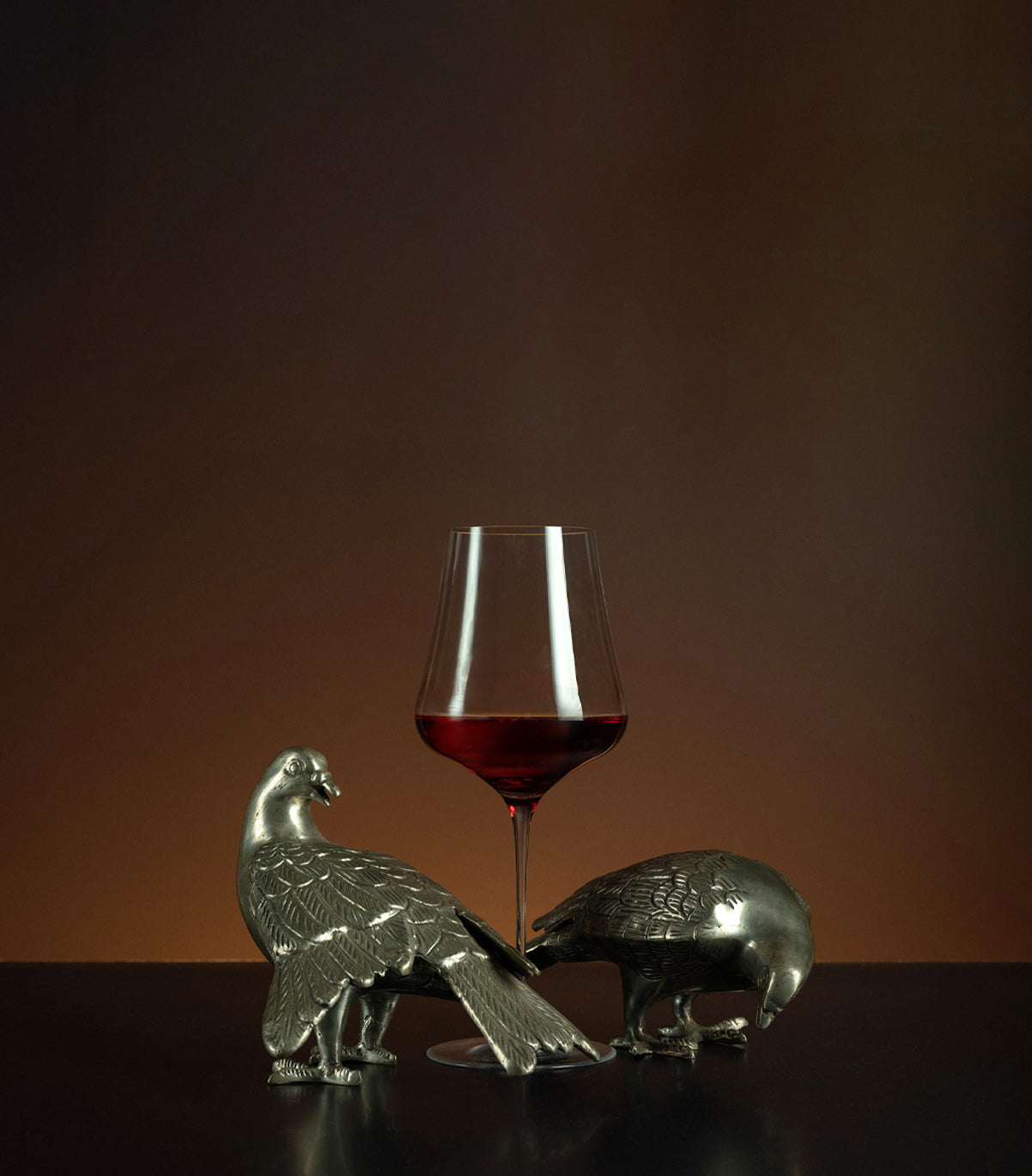 Glass of red wine with animal-shaped metal objects on a dark surface and brown background